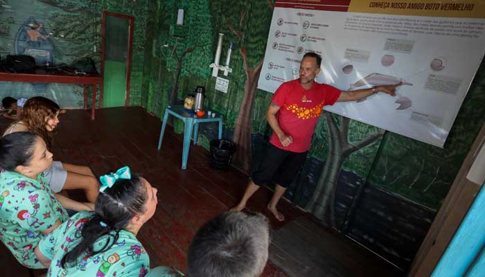 The physiotherapist Igor Simoes Andrade teaches on pink dolphins (Inia Geoffrensis) to young disabled before swimming with them on a boat floating on the Rio Negro river in Iranduba. - AFP