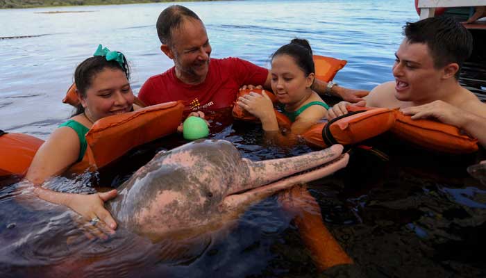 The physiotherapist Igor Simoes Andrade and young disabled people swim with pink dolphins (Inia Geoffrensis) on the Rio Negro river in Iranduba, Amazonas State, Brazil, February 20, 2025. - AFP