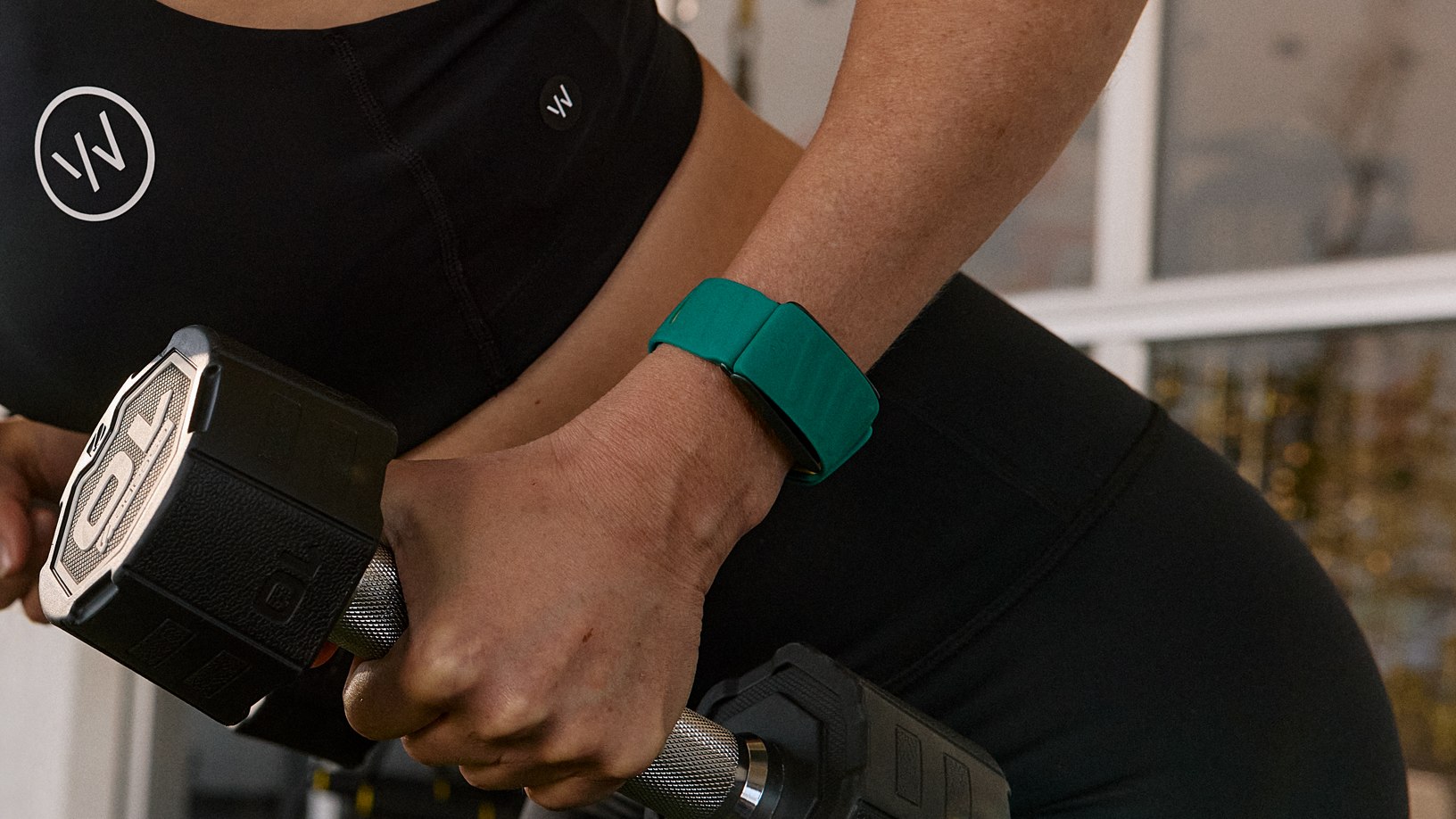 Woman lifting dumbbells while wearing a Whoop wrist device