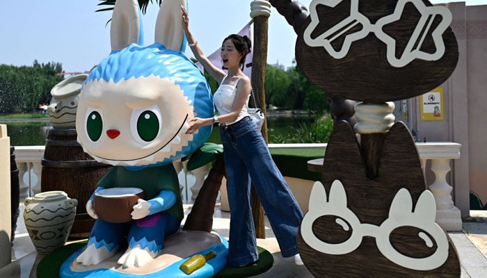 A woman poses for a photo next to the Labu character as she visits the Pop Pop Mirster Pop Themed Park in Beijing, China, June 18, 2025. - AFP
