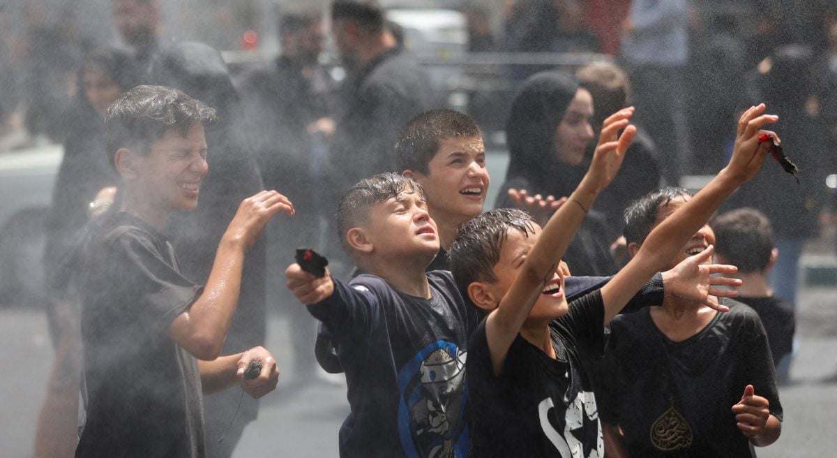 Children cool under water sprinkles as they attend a ceremony to mark Ashura in Tehran, Iran, July 6, 2025. - Reuters