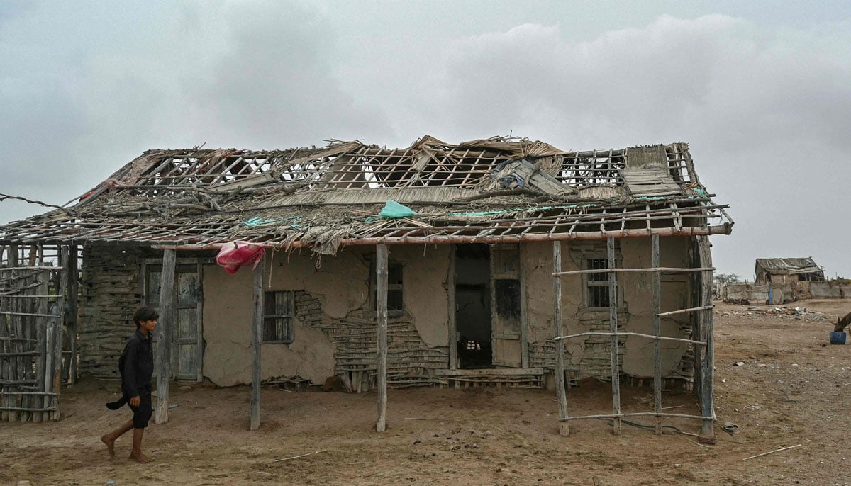 A boy passes in front of an abandoned house in one of the villages in the city of Kharo Chan, in the Inda delta on June 25, 2025. - AFP
