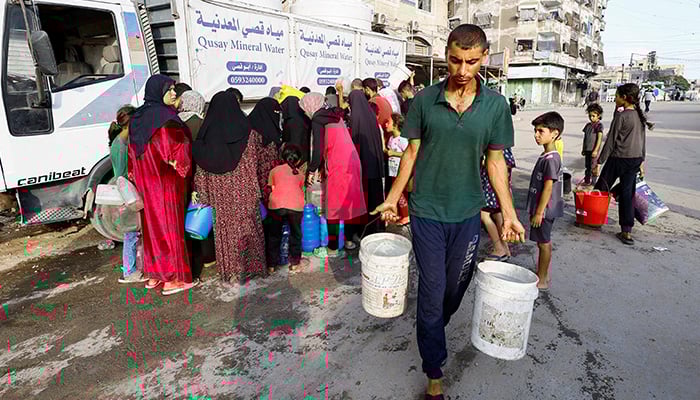 A man carries buckets of water while the Palestinians wait to collect water in the middle of the shortages, in Gaza City on August 6, 2025. - Reuters