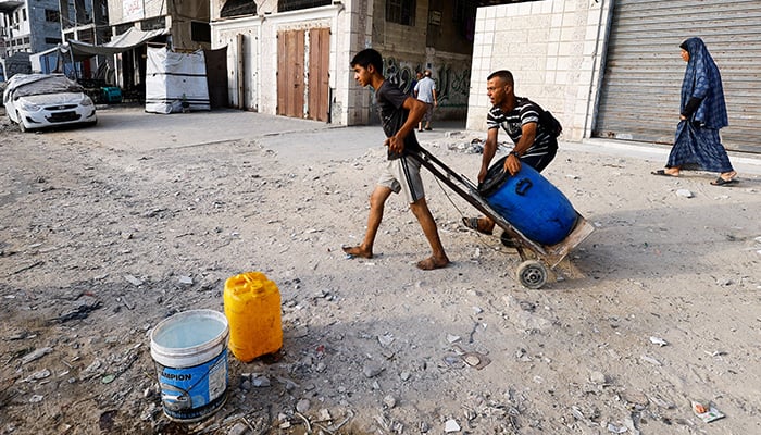 A boy draws a container on a cart while the Palestinians wait to collect water in the middle of the shortages in the middle of shortages, in Gaza City on August 6, 2025. - Reuters