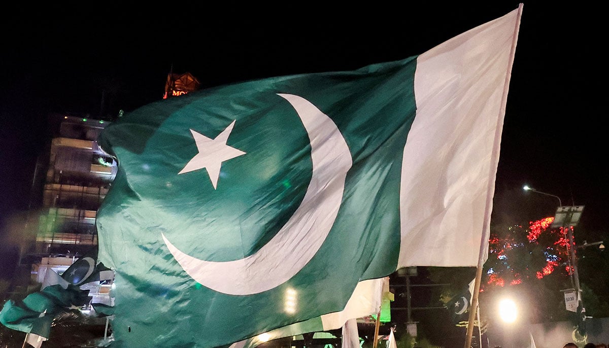People agitate national flags as they meet on the eve of the day of independence in Lahore on August 13, 2025. - Reuters