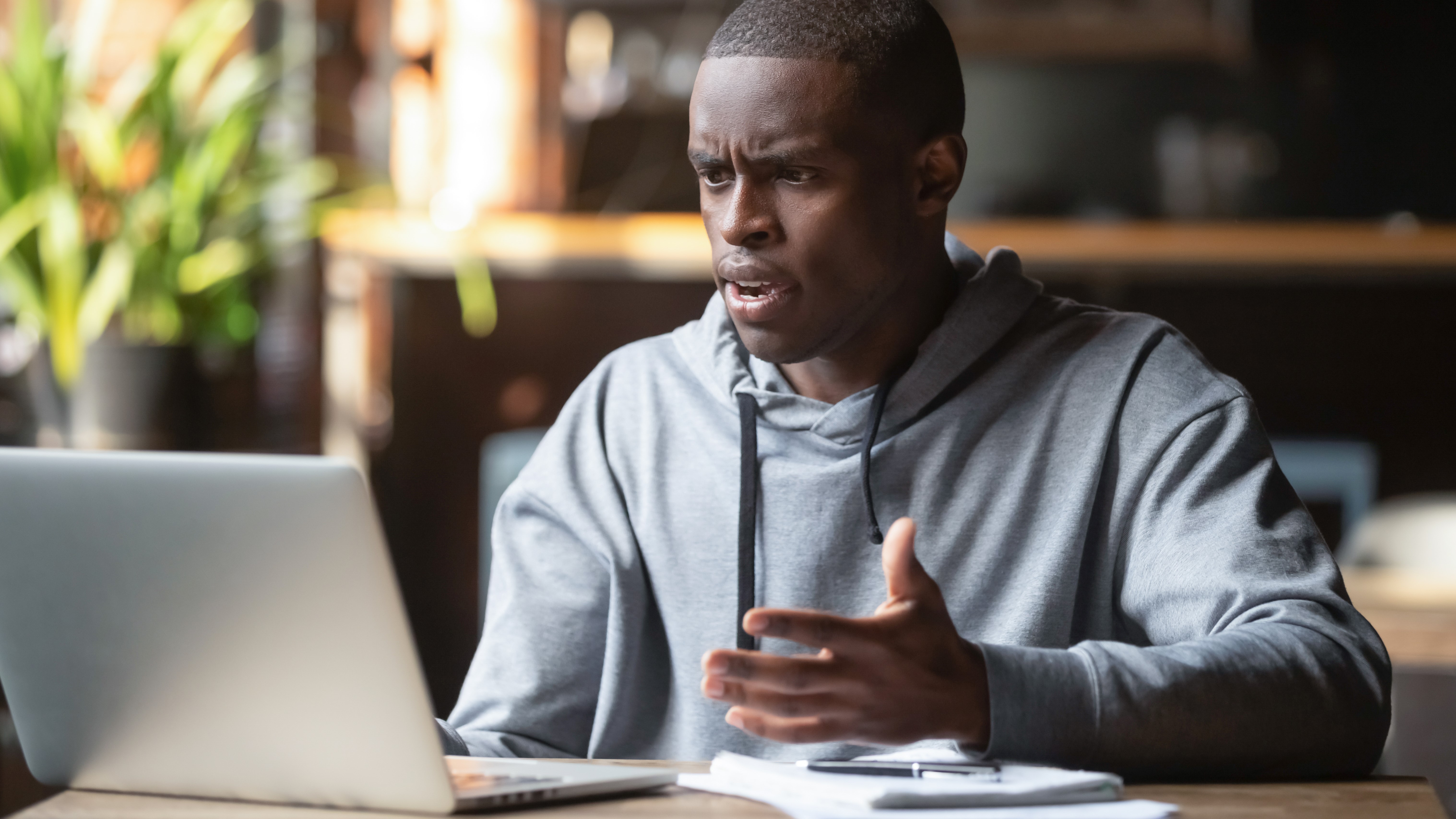 A man with an office using a laptop and raising his hand, while having a confused look on his face