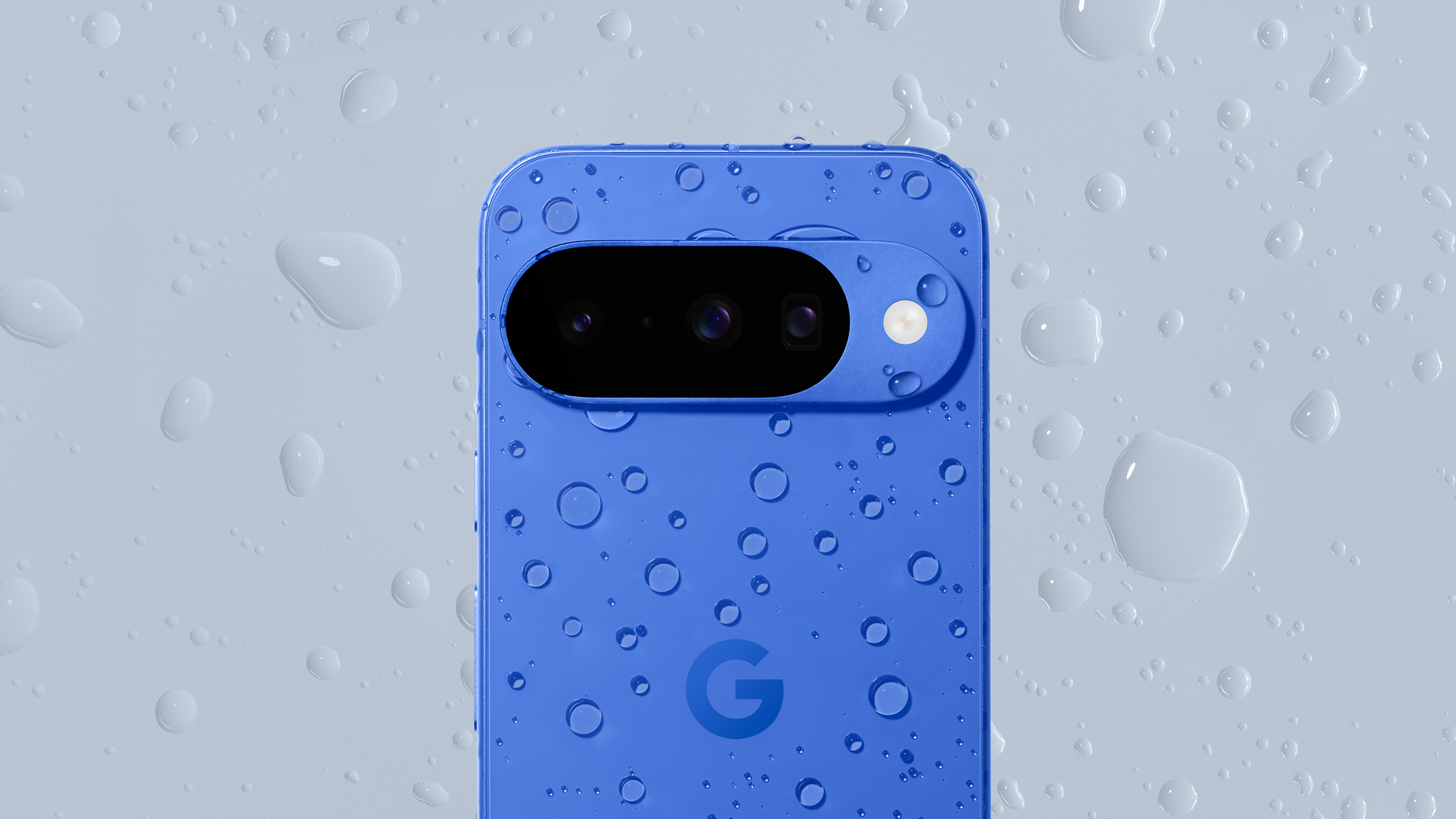 A Blue Indigo version of the Google Pixel 10 phone covered with water droplets on gray background