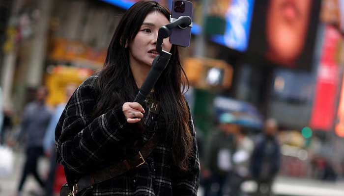 A woman makes a video with a mobile phone to publish on Tiktok while she is held in Times Square in New York, New York, United States, March 13, 2024. - Reuters