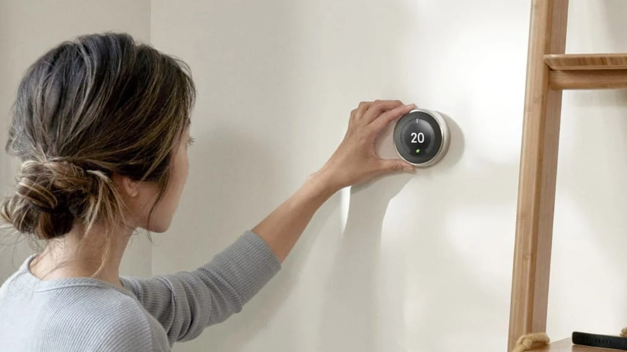 The nest learning thermostat mounted on a wall controlled by a woman