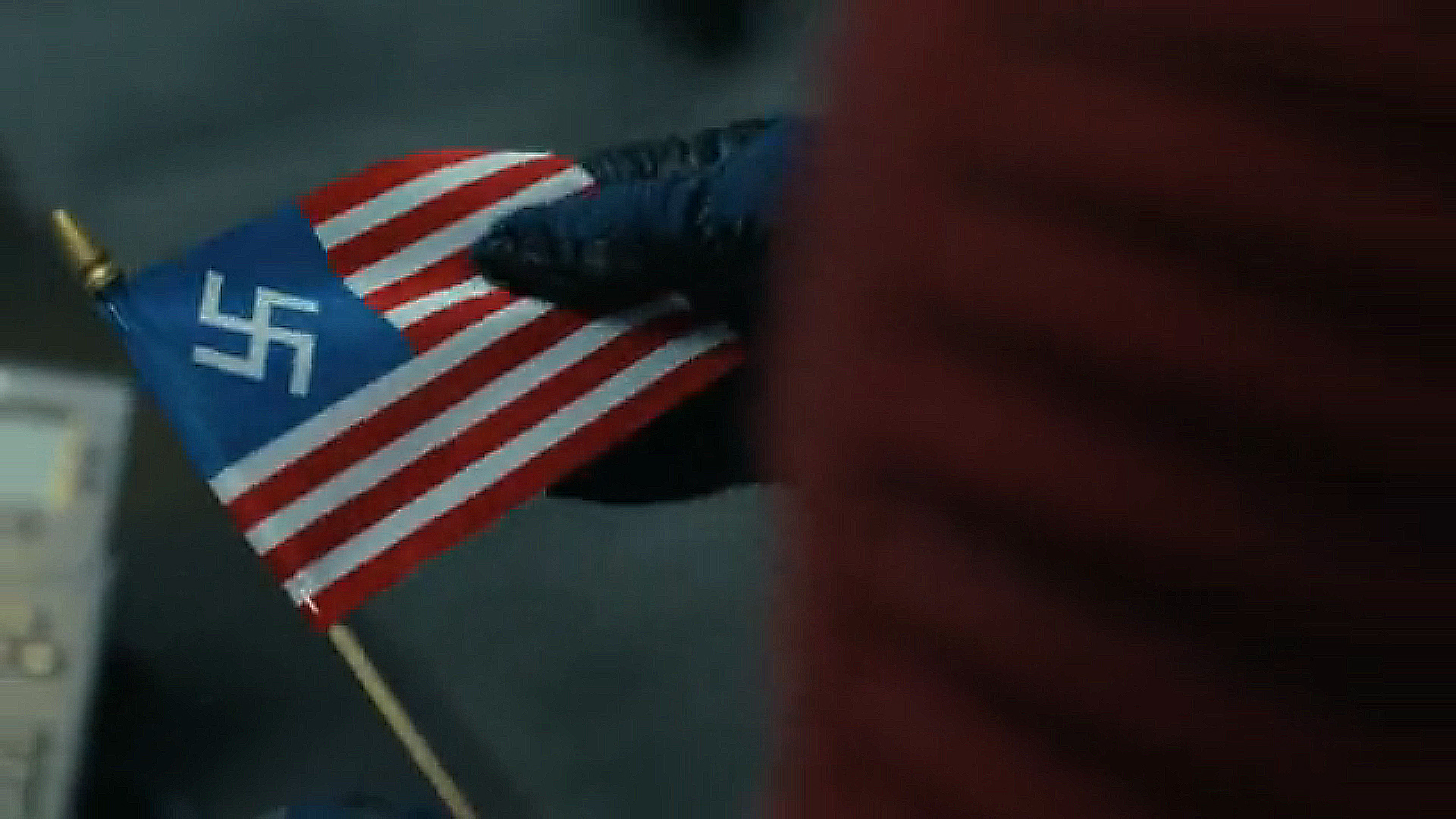 A close -up of Chris Smith holding an American Nazi flag in Peacemaker Season 2 Episode 6