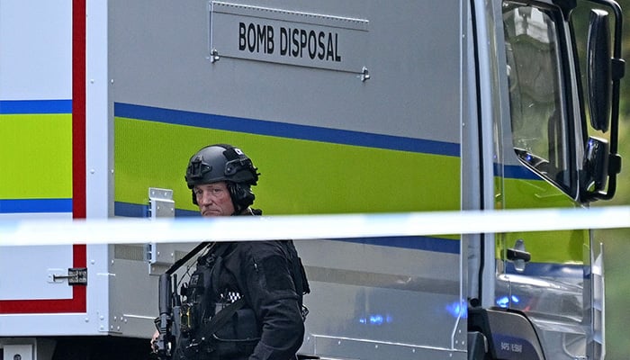 An armed police officer passes in front of an elimination van of the bomb outside the Heaton Park's Hebrew Congregation synagogue in Crumpsall, in the north of Manchester, on October 2, 2025, following a synagogue attack. - AFP