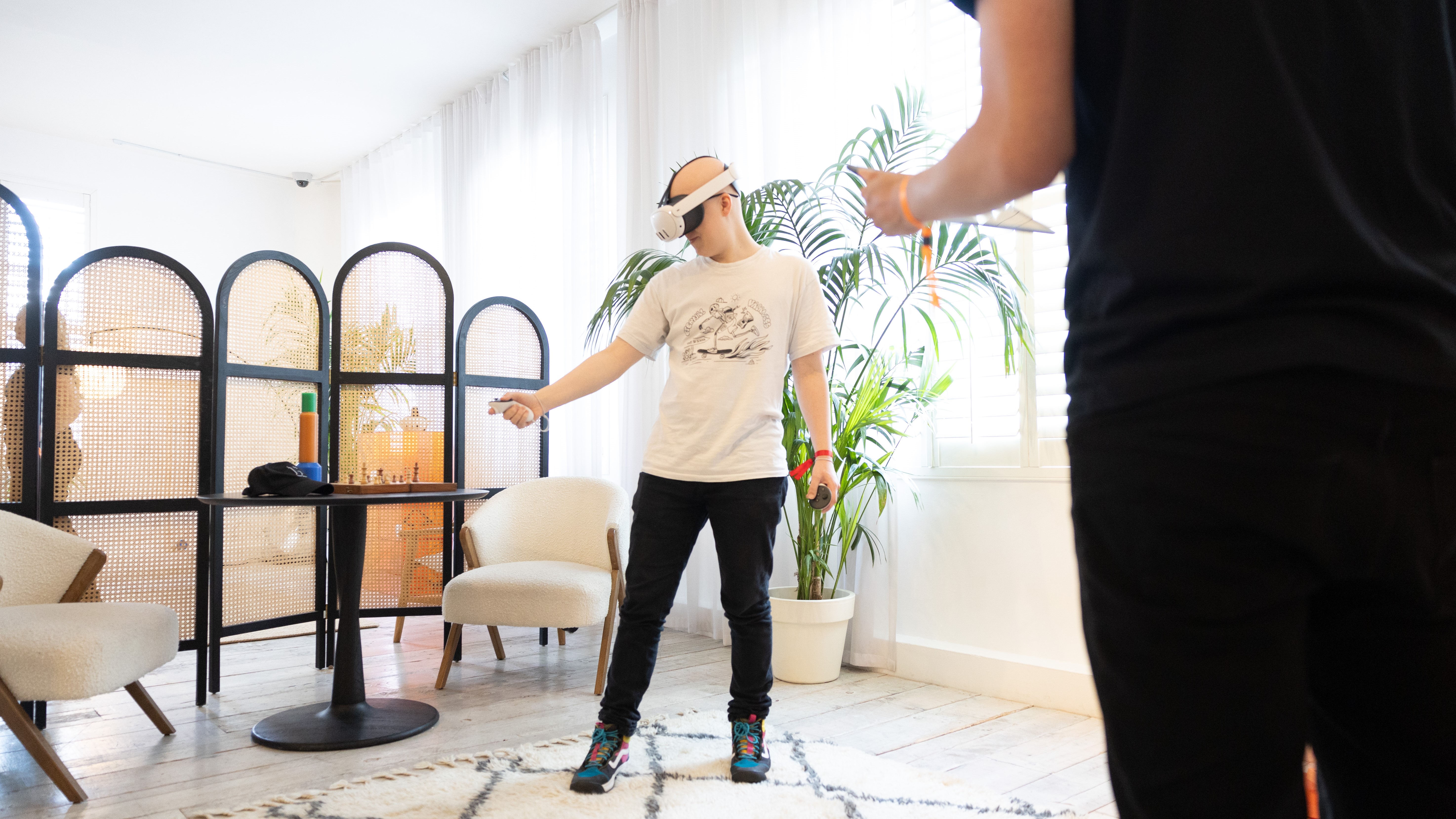 Hamish interacting with VR objects while wearing a meta quest 3. They stand in front of a plant while someone looks.
