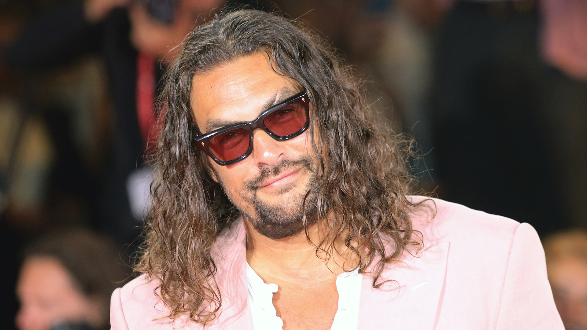 Jason Momoa has sunglasses and poses for photos on a red carpet
