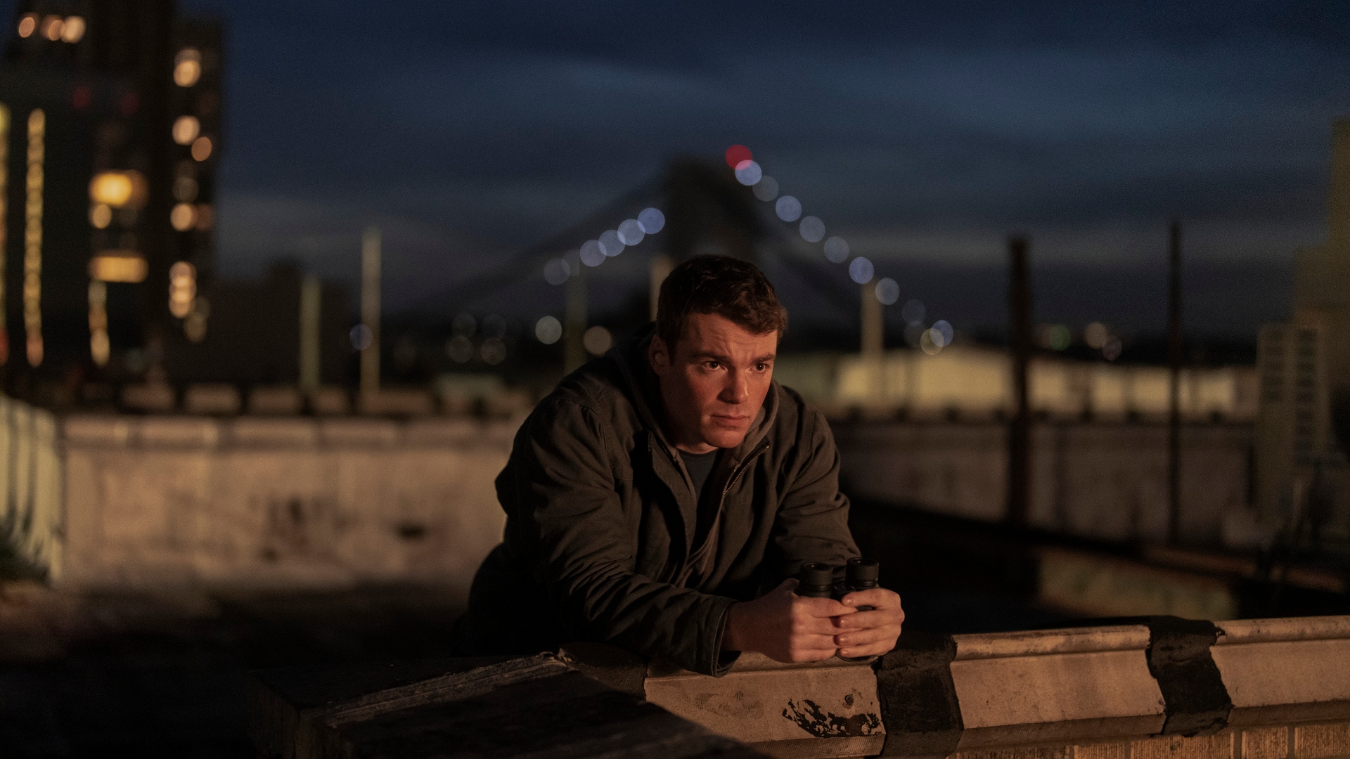 Peter leans on a bridge at night in The Night Agent