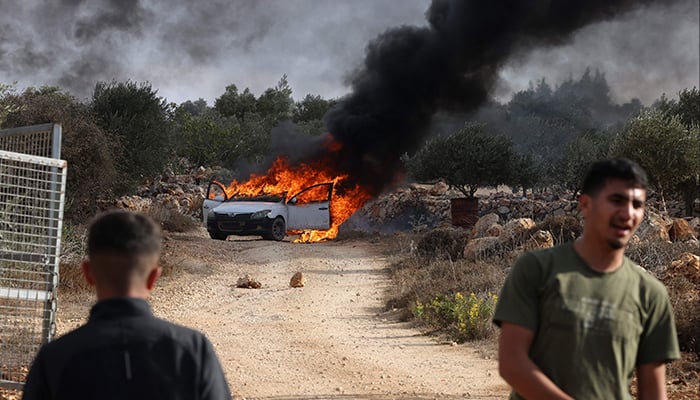 Palestinians stand near a burning car believed to have been set on fire by Israeli settlers who tried to disrupt them harvesting olives near the occupied village of Turmos Ayya, near Ramallah, in the West Bank, October 19, 2025. — AFP