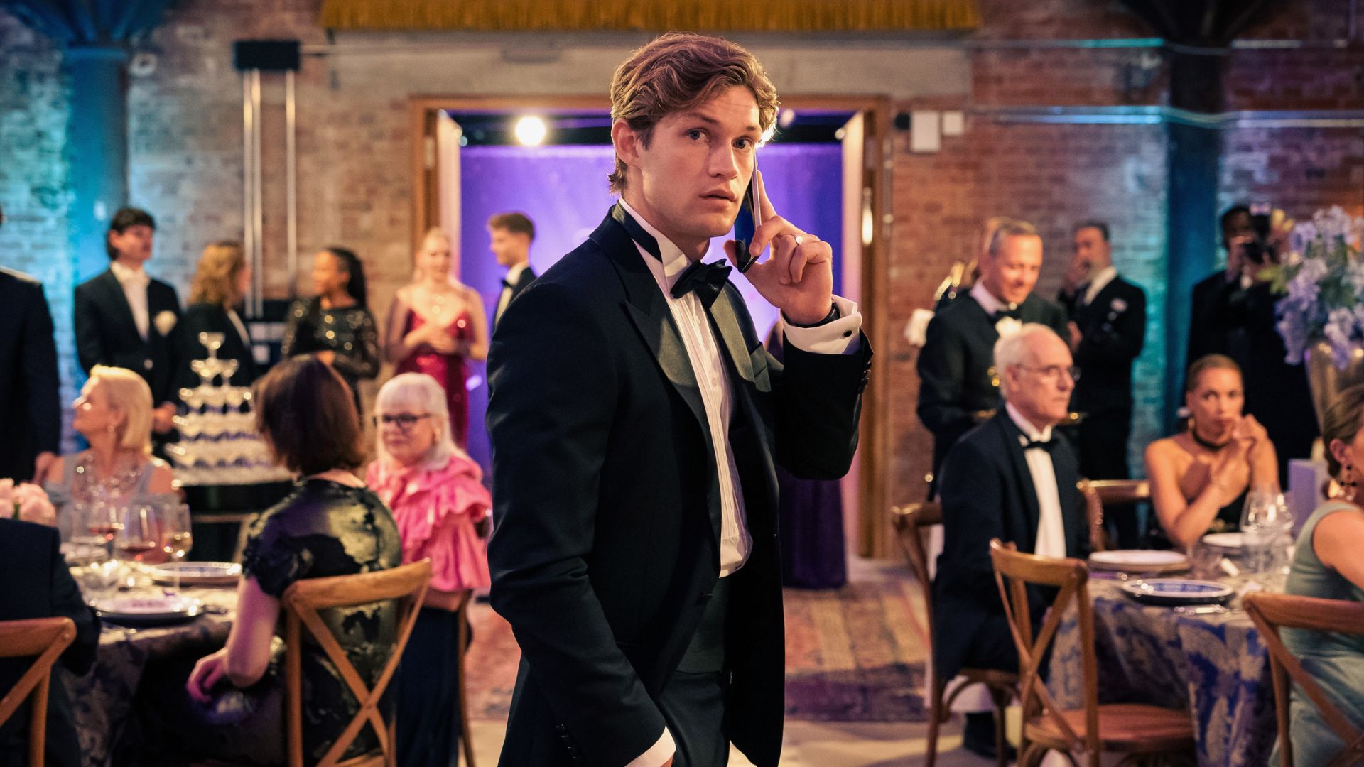 James holds a phone to his ear in the middle of a seated crowd.