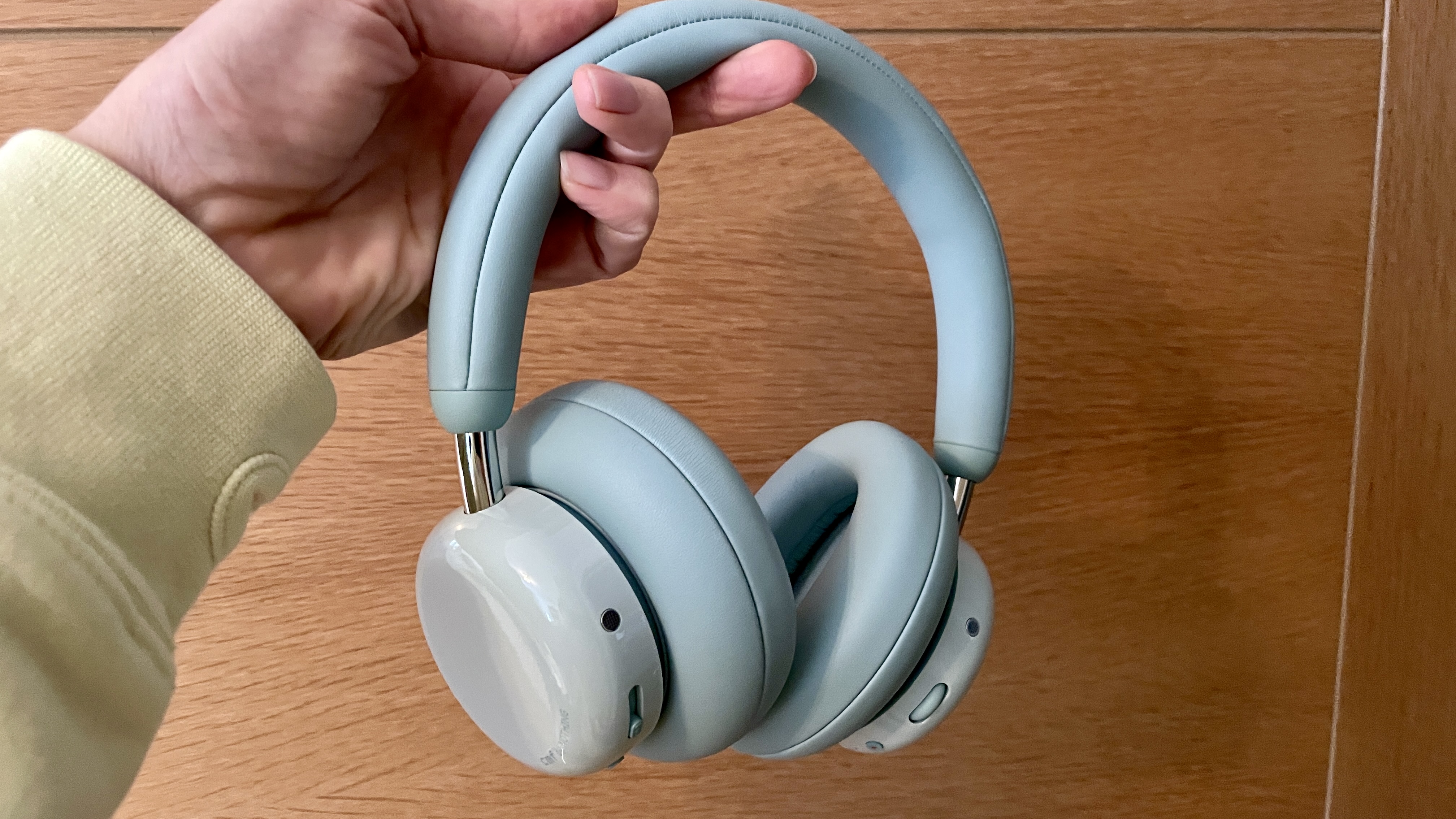 CMF Headphone Pro pistachio green held in one hand or hung on a bar, pushed upwards by a sculpted frog