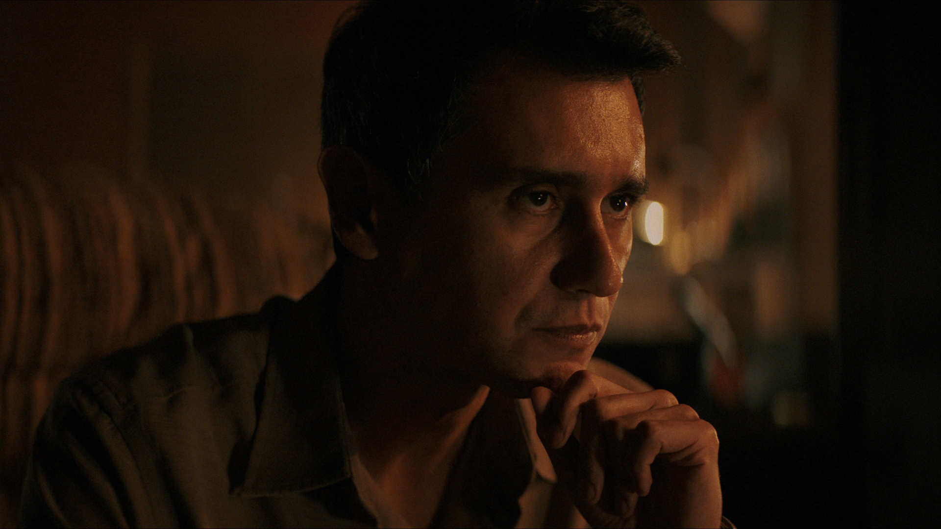 Manusos rests his chin on his left hand in episode 4 of Pluribus