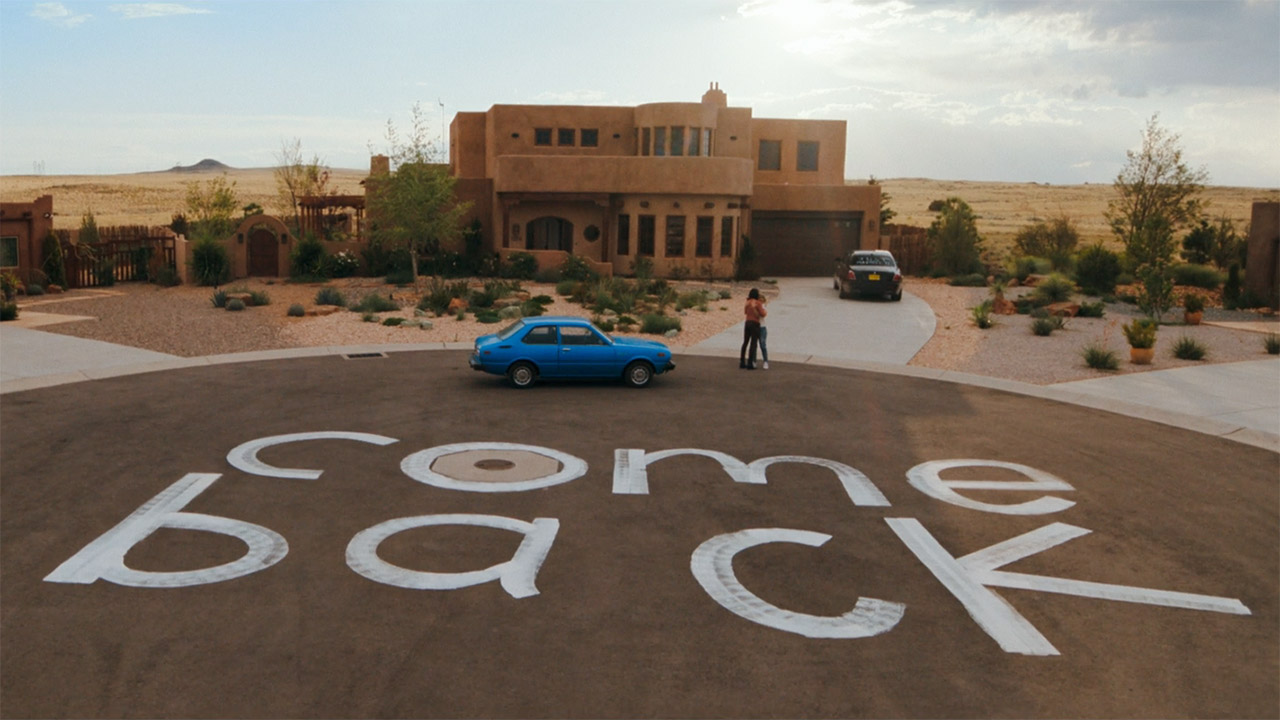 A wide shot of Zosia and Carol hugging near a giant painted sign 
