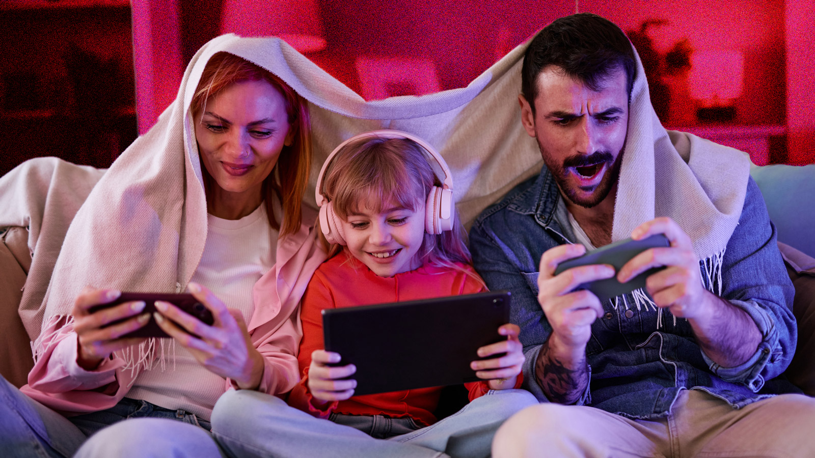 Young family sitting on a couch, all using phones and looking excited.