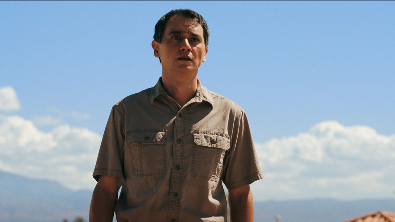 Manousos standing in front of Carol's house in episode 9 of Pluribus