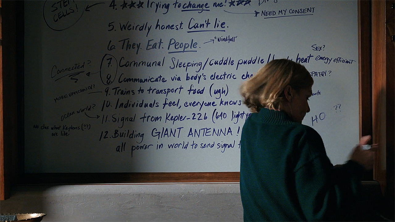 Carol standing in front of a whiteboard with information about the Others written on it in episode 8 of Pluribus
