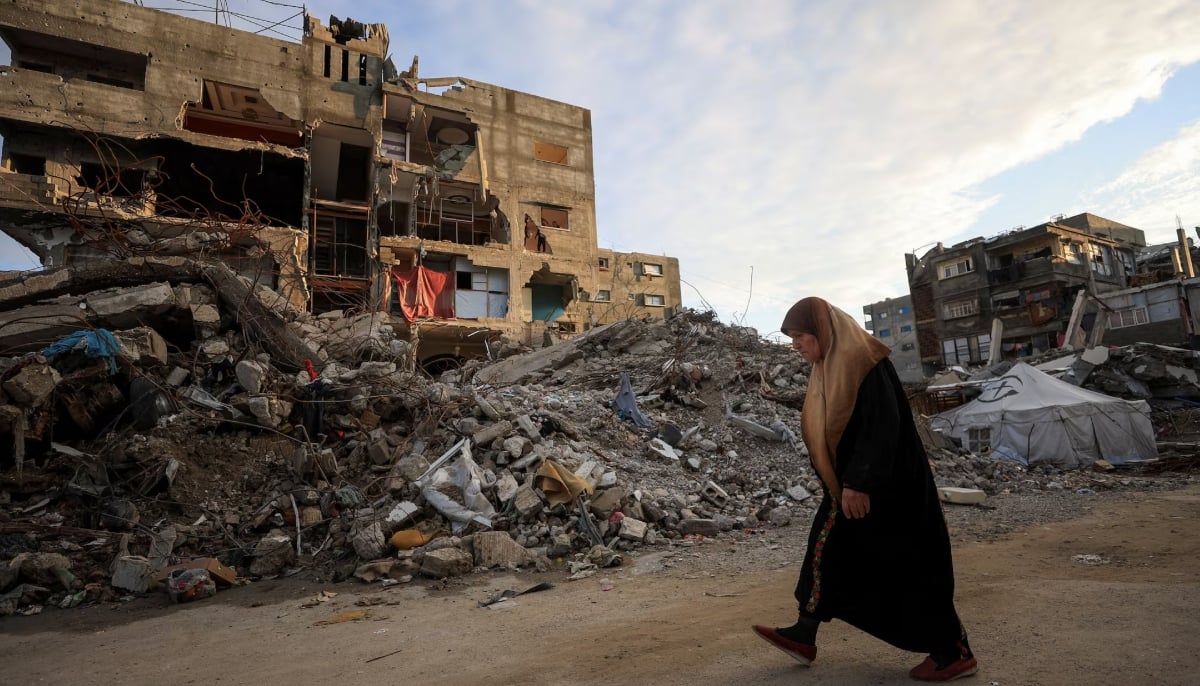 A Palestinian woman walks past residential buildings damaged and destroyed during the war, in Gaza City, December 14, 2025. — Reuters