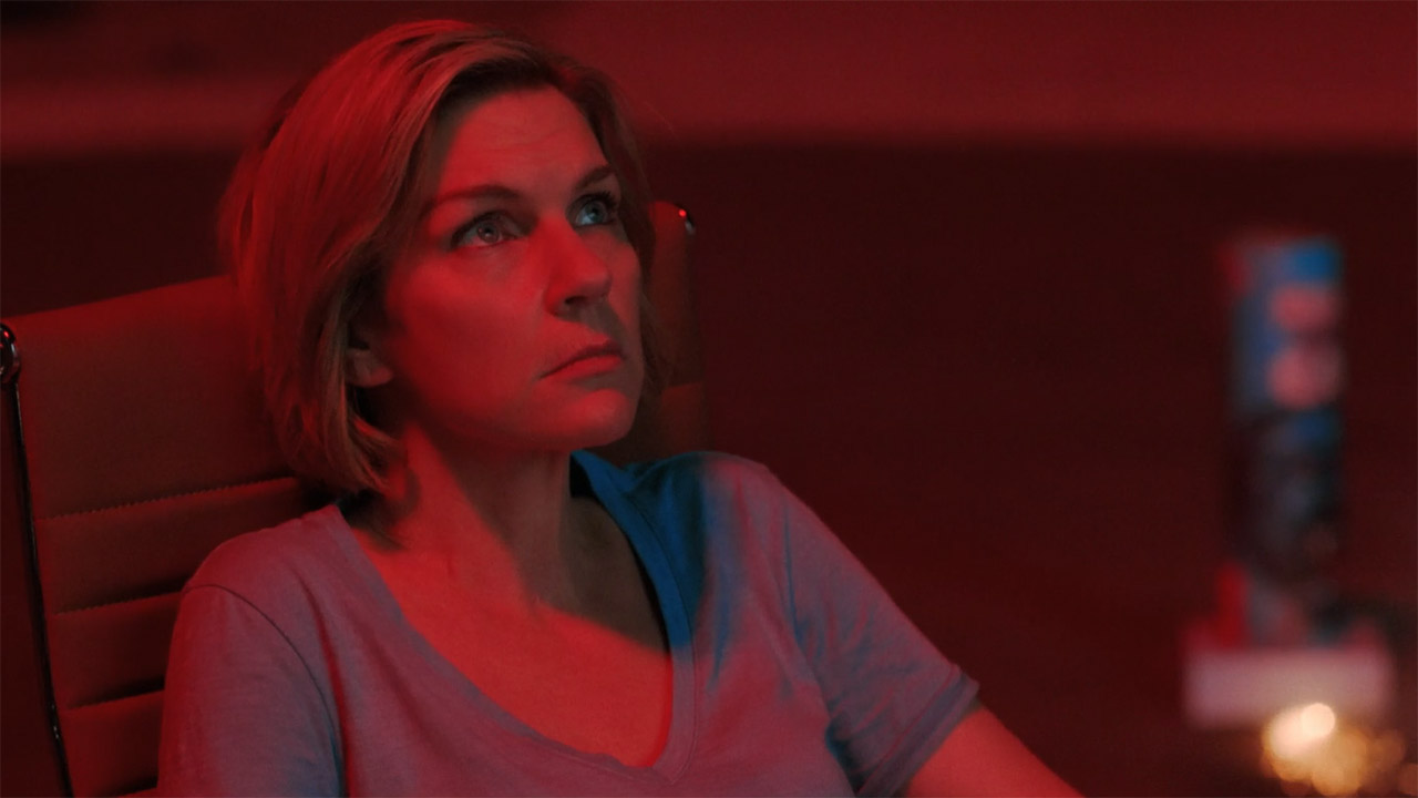 Carol sitting and bathed in red light from fireworks at night in episode 7 of Pluribus