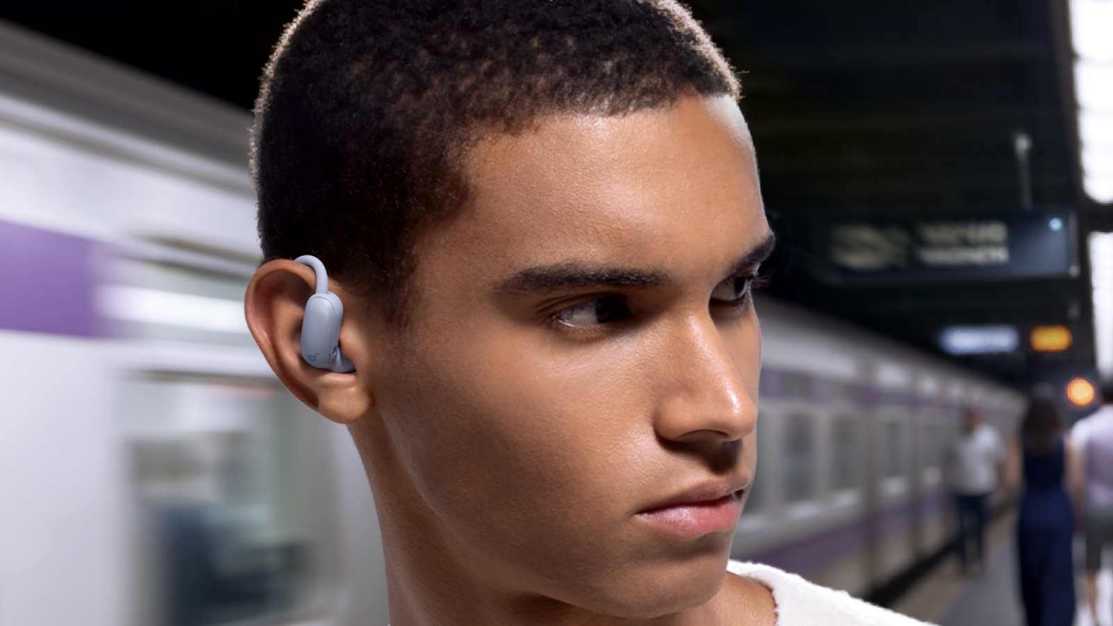 The Anker Soundcore Aerofit 2 Pro in a man's ear as he looks the wrong way to wait for the train.