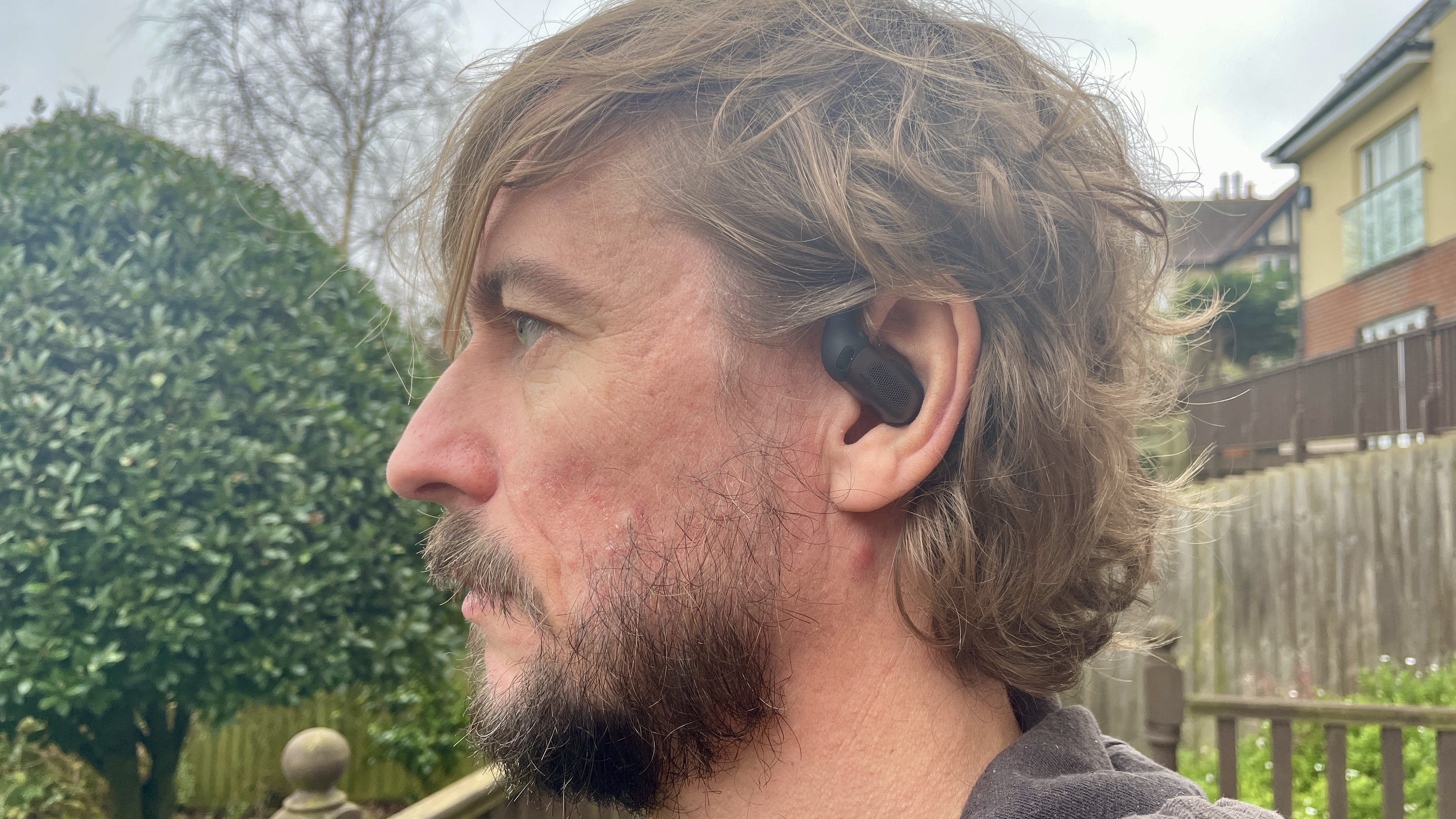 Shokz Openfit Pro outdoors, held outdoors in a woman's hand, with green grass in the background