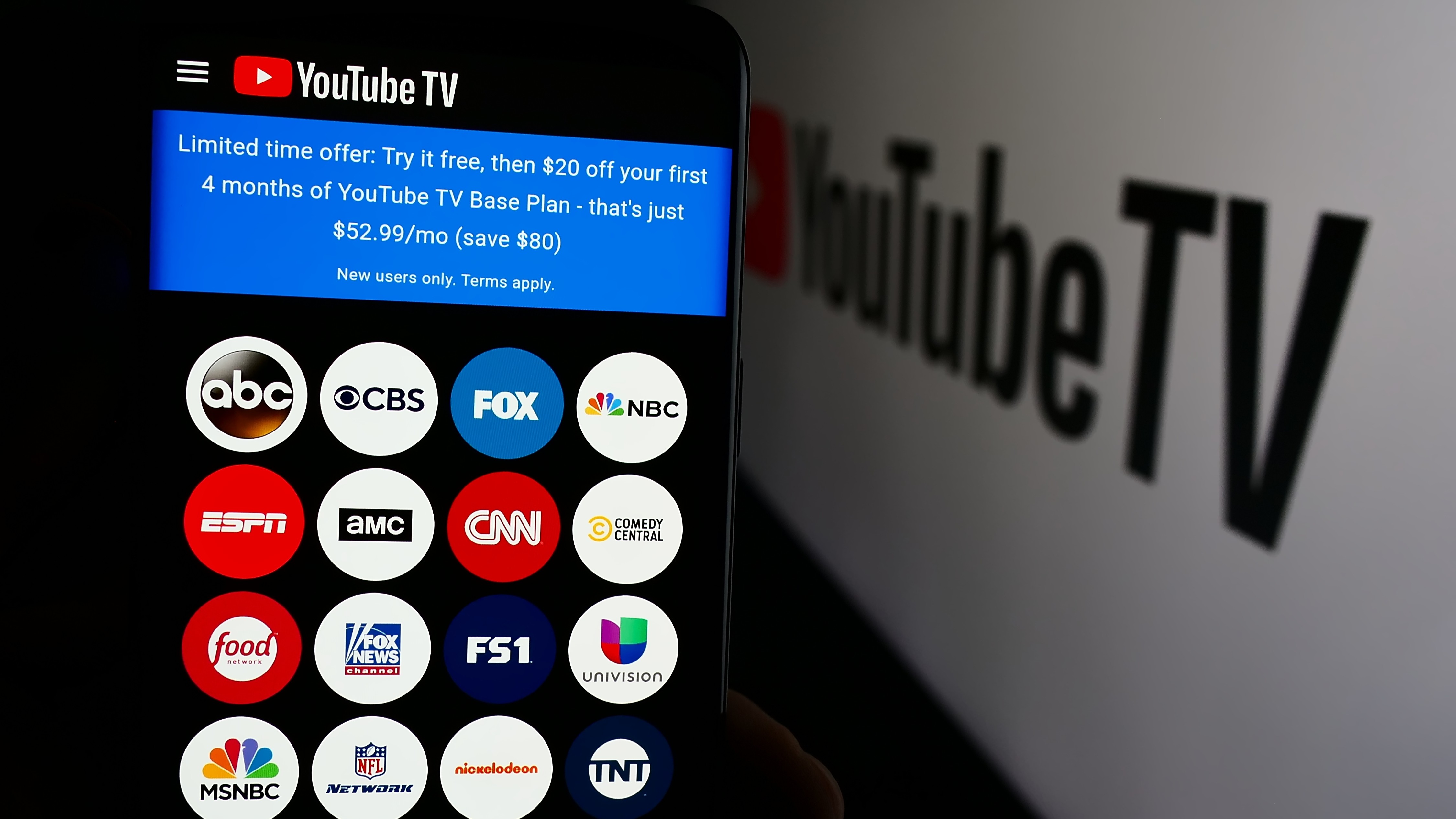 Person holding cell phone with YouTube TV webpage in front of company logo.