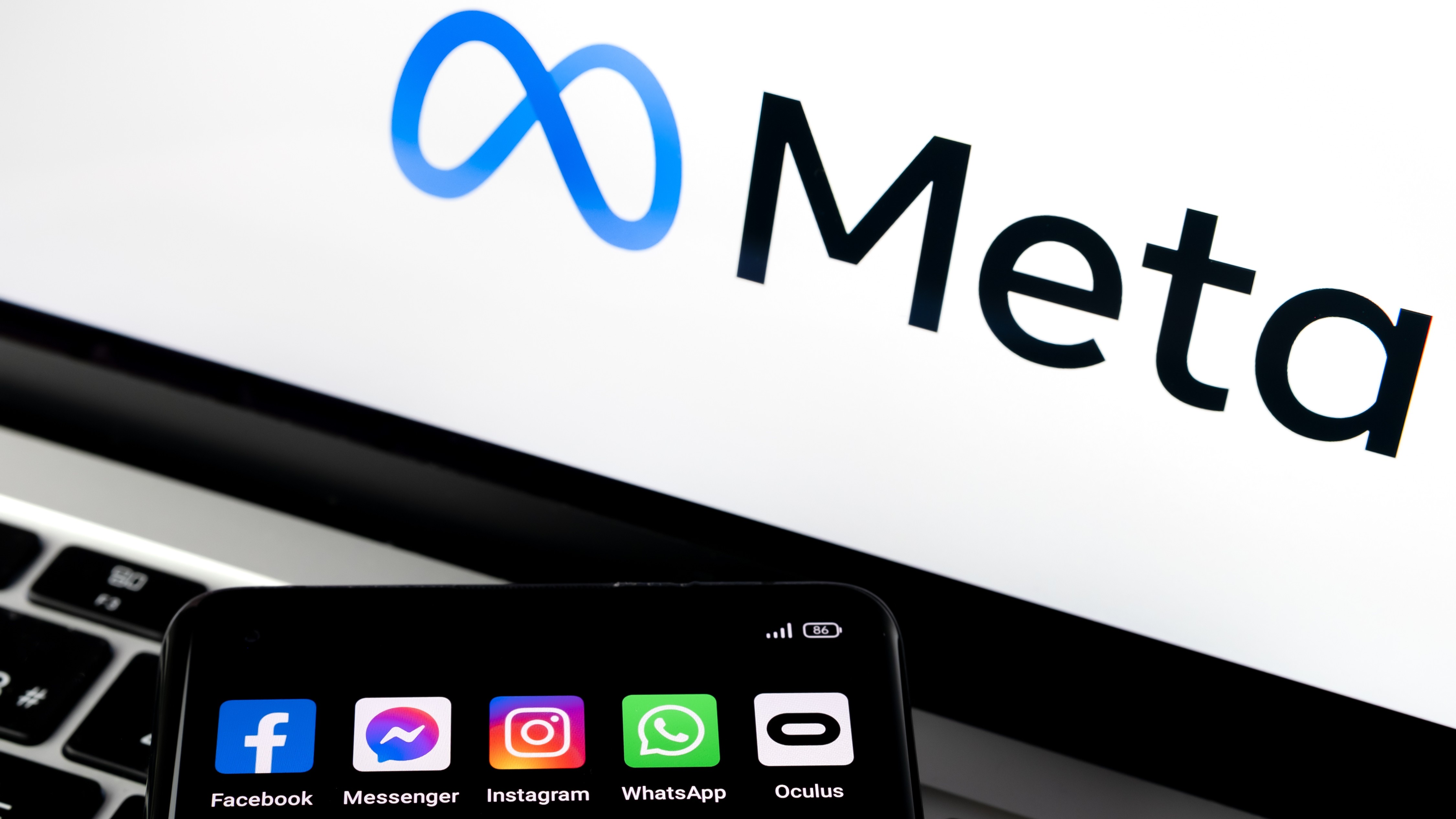Smartphone silhouette with Facebook, Messenger, WhatsApp, Instagram, Oculus apps and blurred META logo in background