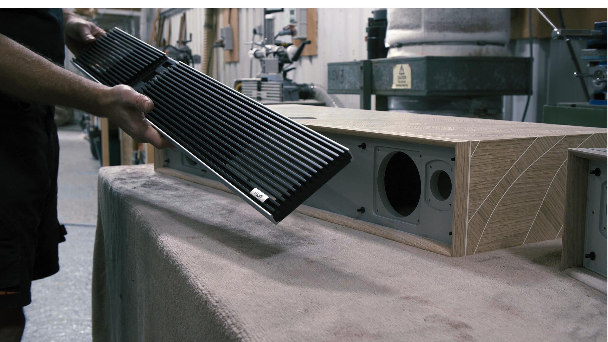 Ruark R810 MiE hand-assembled in the Ruark factory. A person holds a dark rack in front of an R810 MiE cabinet