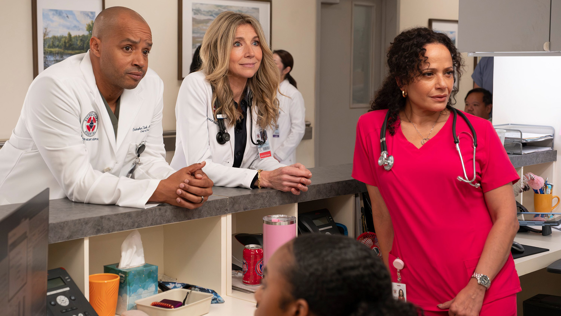 Turk and Elliot lean at the front desk behind Carla in the Scrubs revival.