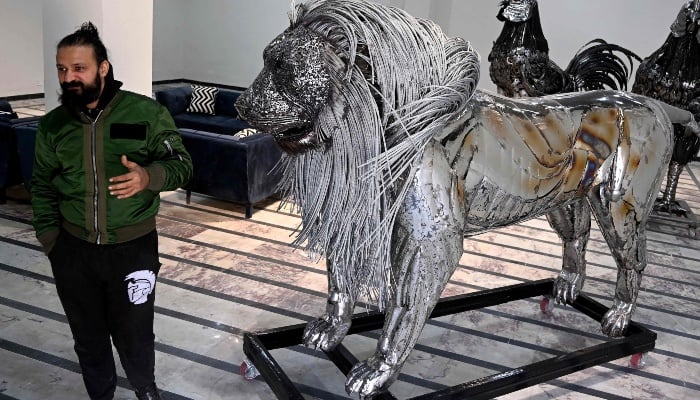 This photograph, taken on December 29, 2025, shows sculptor Ehtisham Jadoon standing next to his creation made from scrap metal, a lion with a twisted steel mane, in his workshop on the outskirts of Islamabad. -AFP