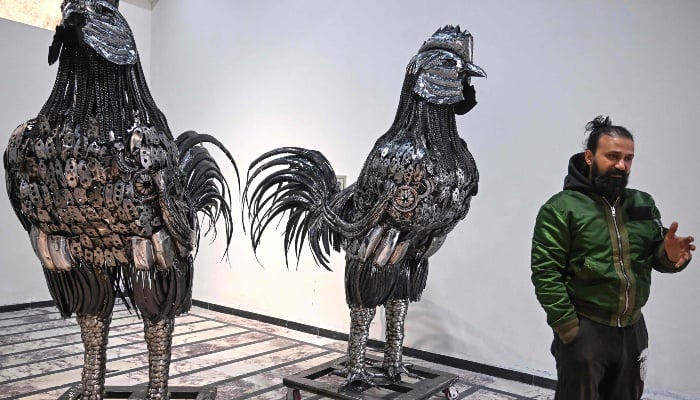 This photograph, taken on December 29, 2025, shows sculptor Ehtisham Jadoon standing next to rooster sculptures made from scrap metal in his workshop on the outskirts of Islamabad. -AFP
