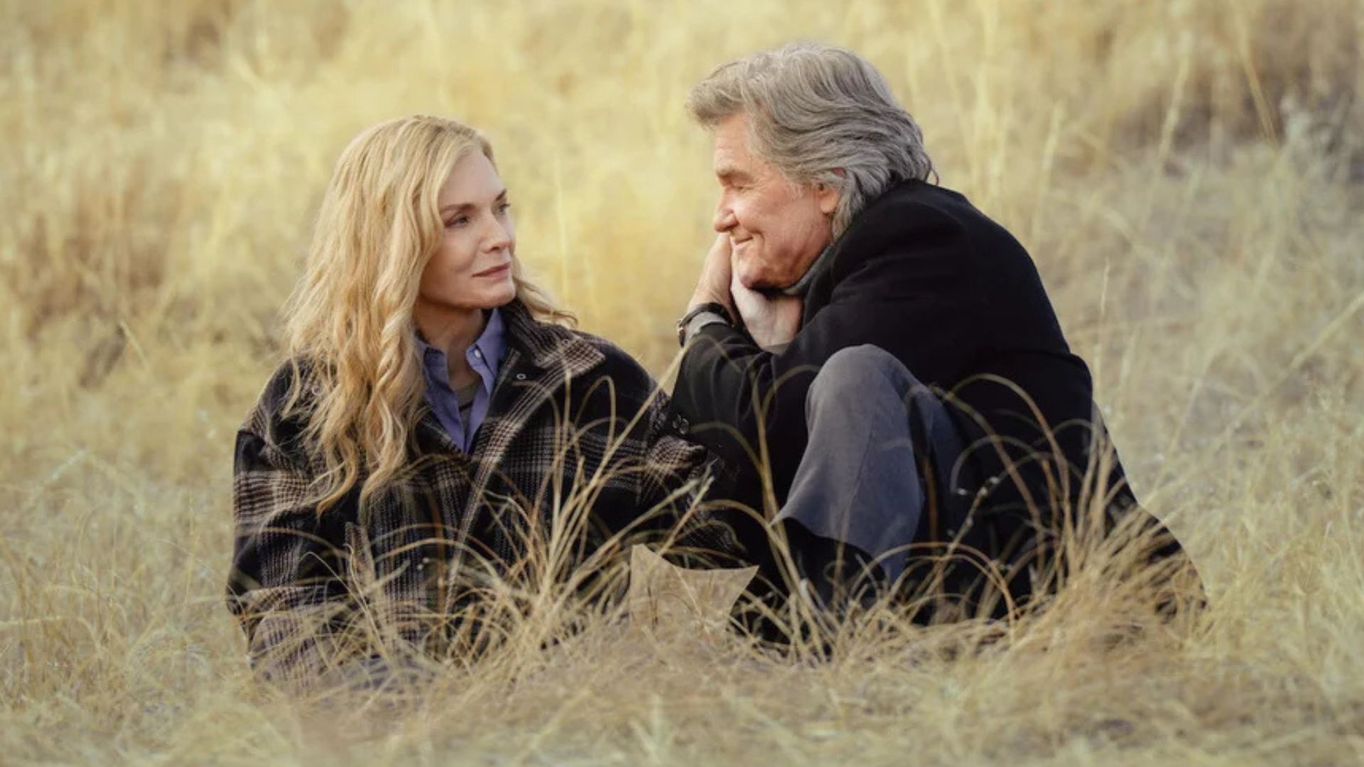 Michelle Pfeiffer and Kurt Russell are sitting in the middle of a grassy field
