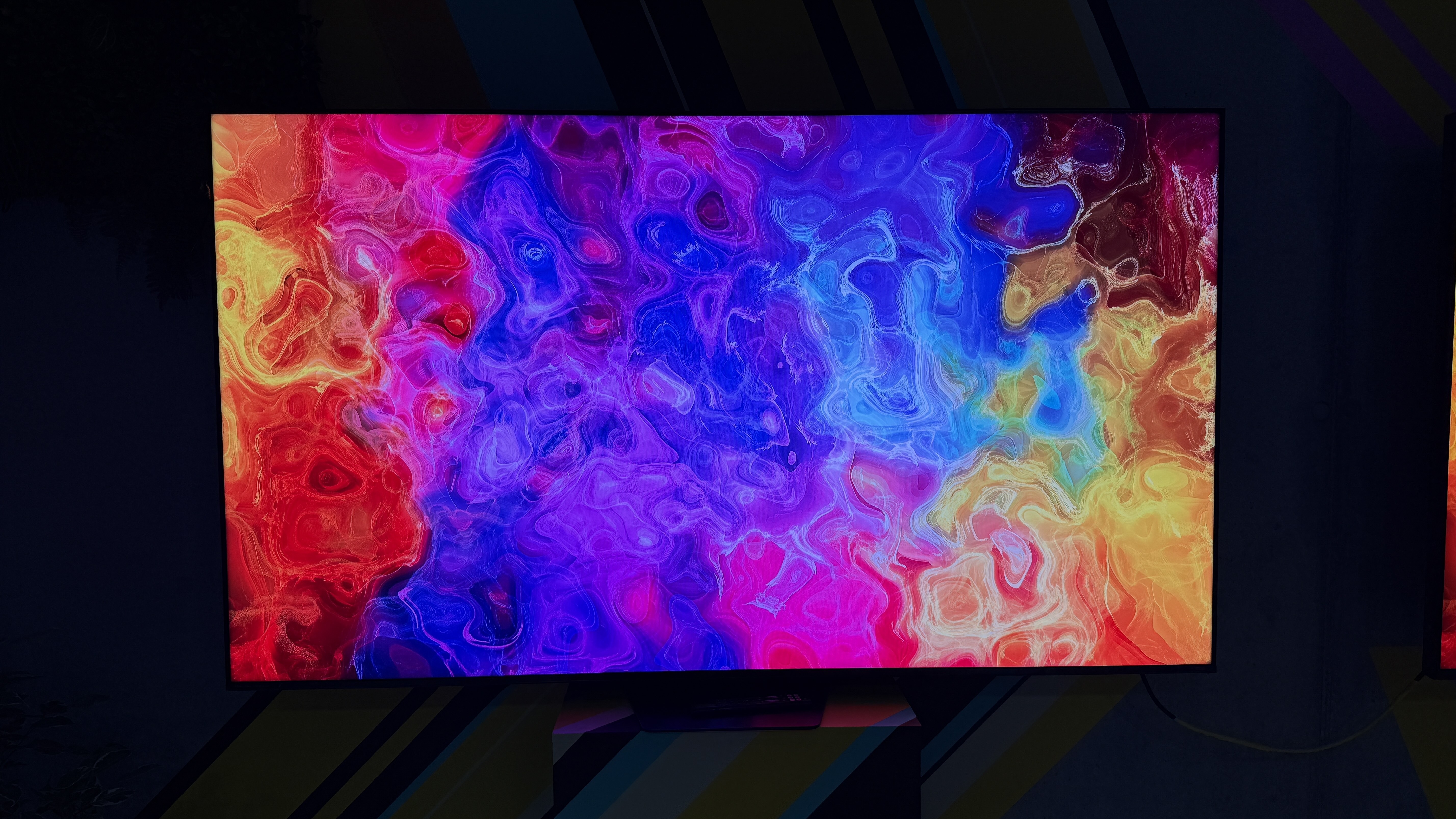 The Hisense UR9S RGB TV in a dark room, with a rippling color pattern on the screen showing off its impressive color reproduction
