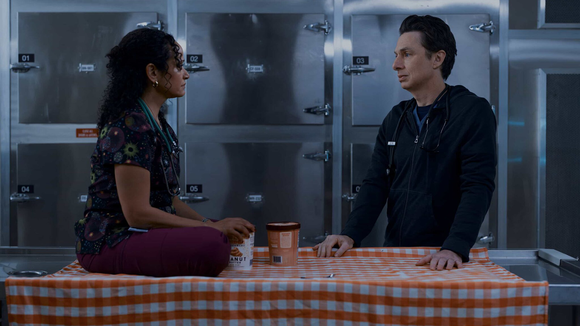 Carla sitting cross-legged on a table next to which JD stands in Scrubs season 10 episode 7