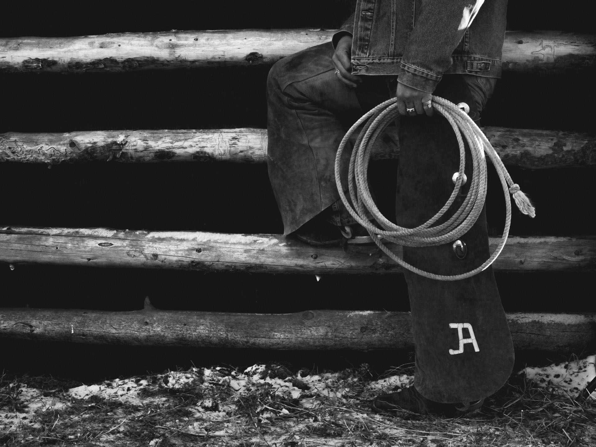Black and white image of a cowboy model's legs, they are holding a rope