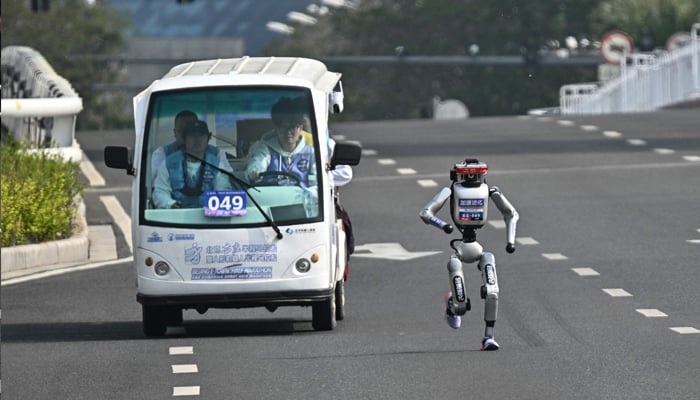 A robot and its engineers participate in the second E-Town half marathon and humanoid half marathon in Beijing, April 19, 2026. — AFP