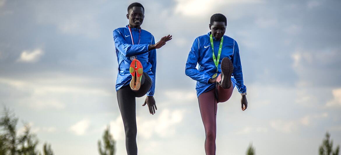 Two young African athletes in blue tracksuits stretch on a running track at the Teryet National High Altitude Training Center in Uganda. The image is part of a UNFPA documentation effort to highlight how athletics provide safe spaces and build confidence for girls, particularly survivors of female genital mutilation (FGM).
