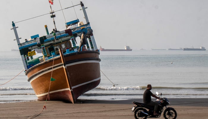 In this photo obtained from Iranian news agency ISNA on April 24, 2026, an Iranian man rides his motorcycle past a boat on Suru Beach in Bandar Abbas, along the Strait of Hormuz. -AFP