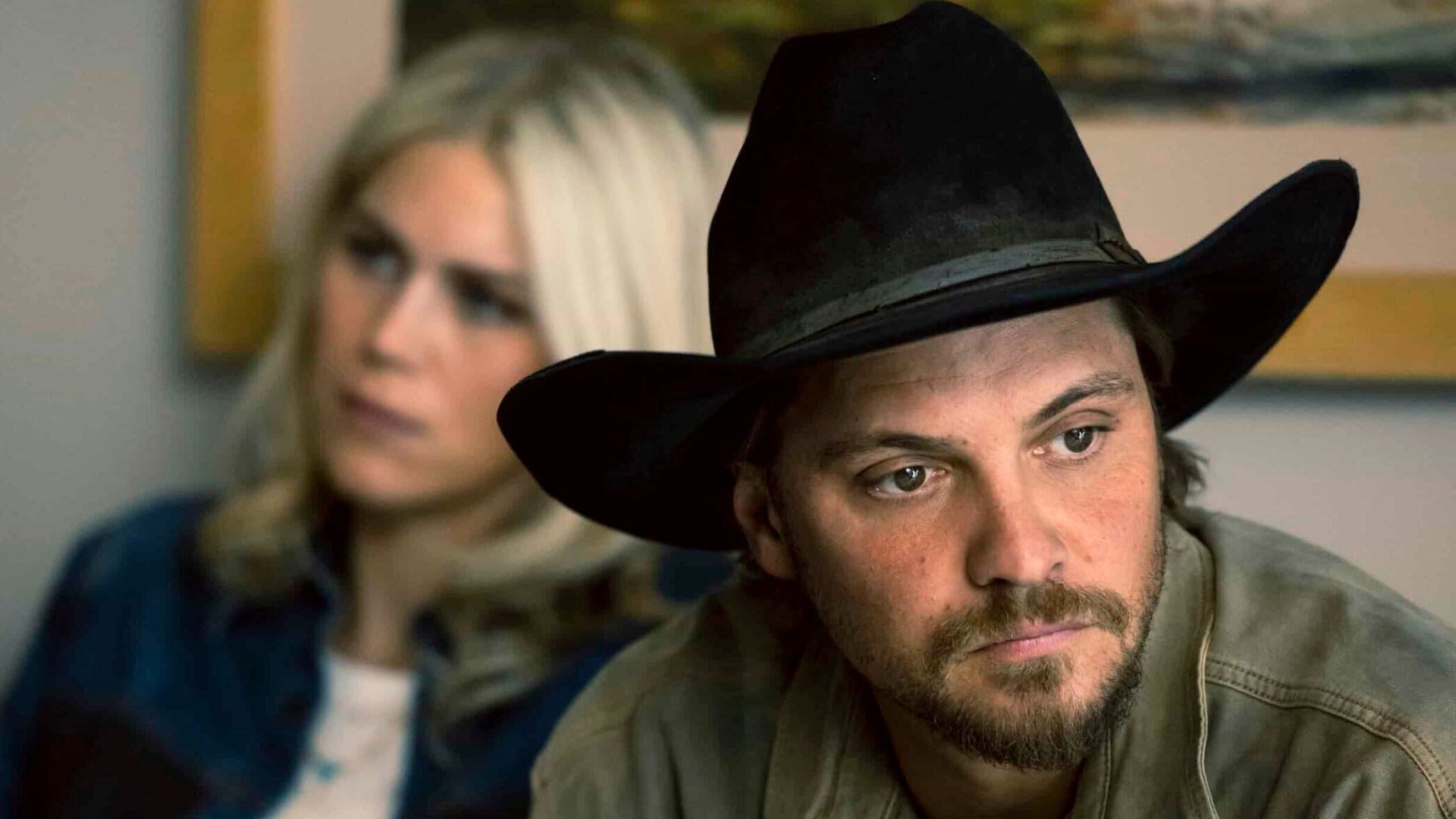 Kayce looks away as a blonde woman sits behind him.