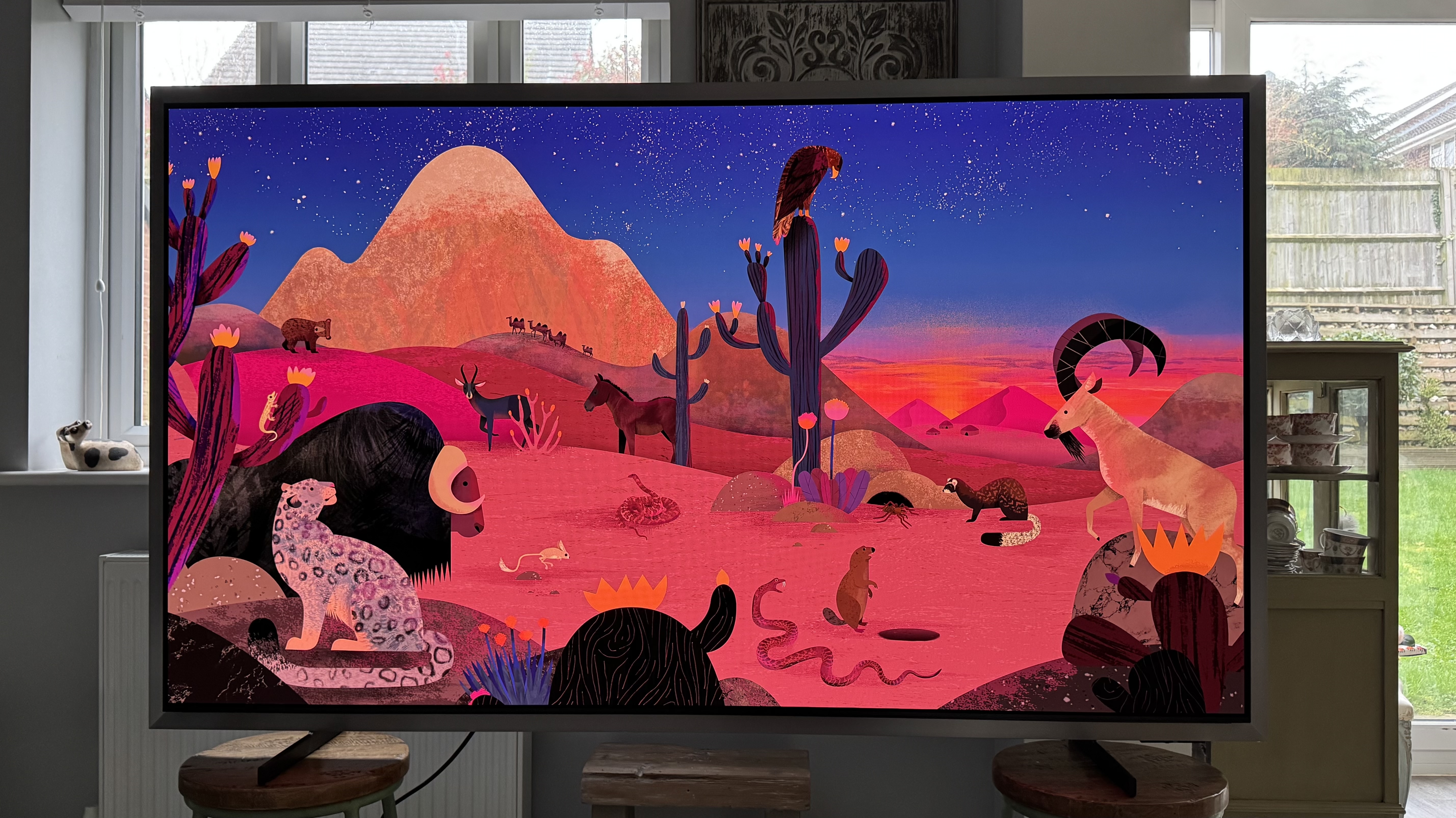 The Samsung S99H/S95H TV in a home, displaying an abstract image of a desert scene on the screen, showing off its punchy colors