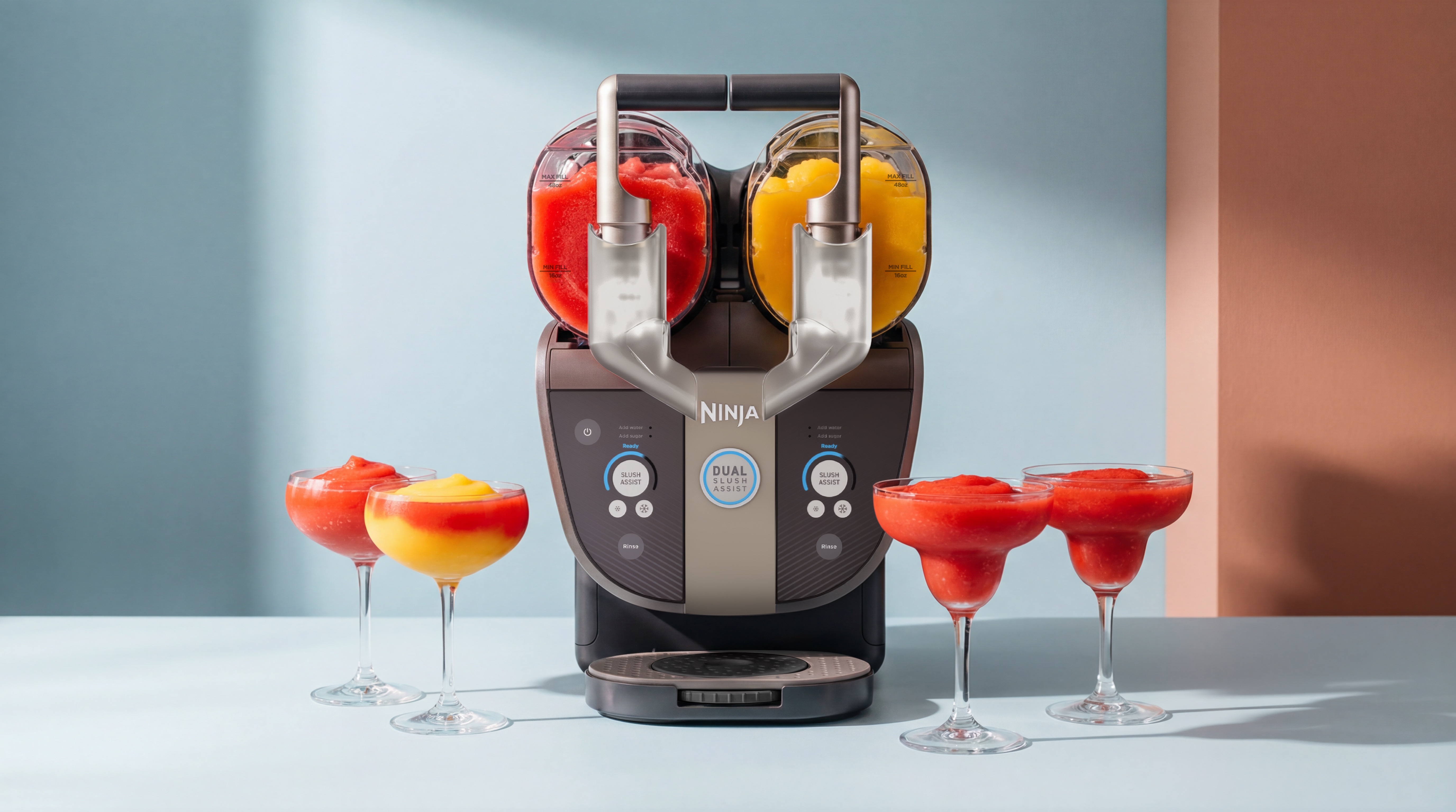 Ninja Slushi Twist on a light colored counter with a red drink in one chamber and a yellow one in the second. There are four brightly colored drinks in cocktail glasses in front.
