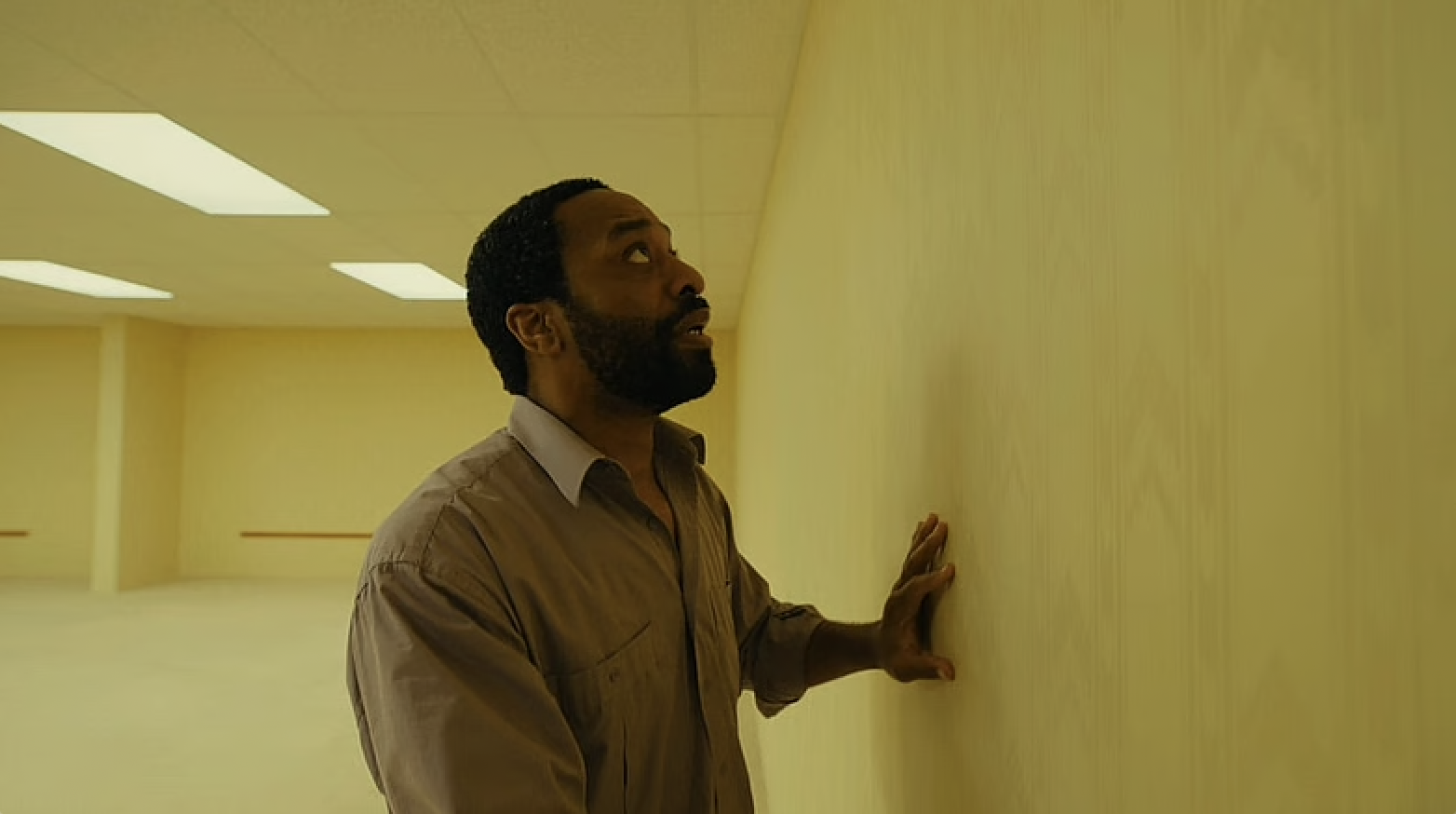 Chiwetel Ejiofor in Backrooms, where he is in an empty yellow room. He touches a wall and looks scared.