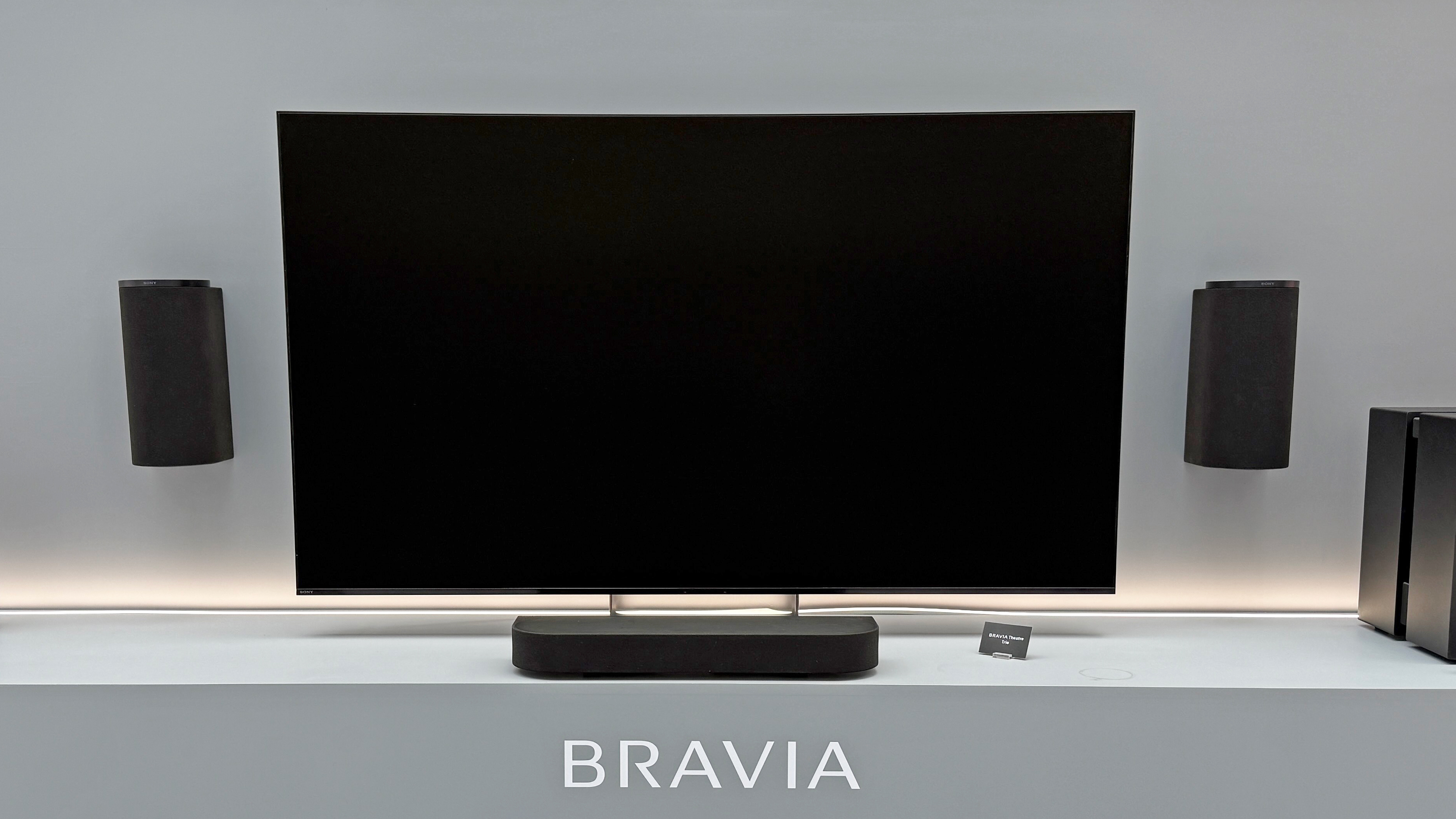 The Sony Bravia Theater Trio with a black television screen. Two speakers hang on the wall, either side of a TV with a small speaker below