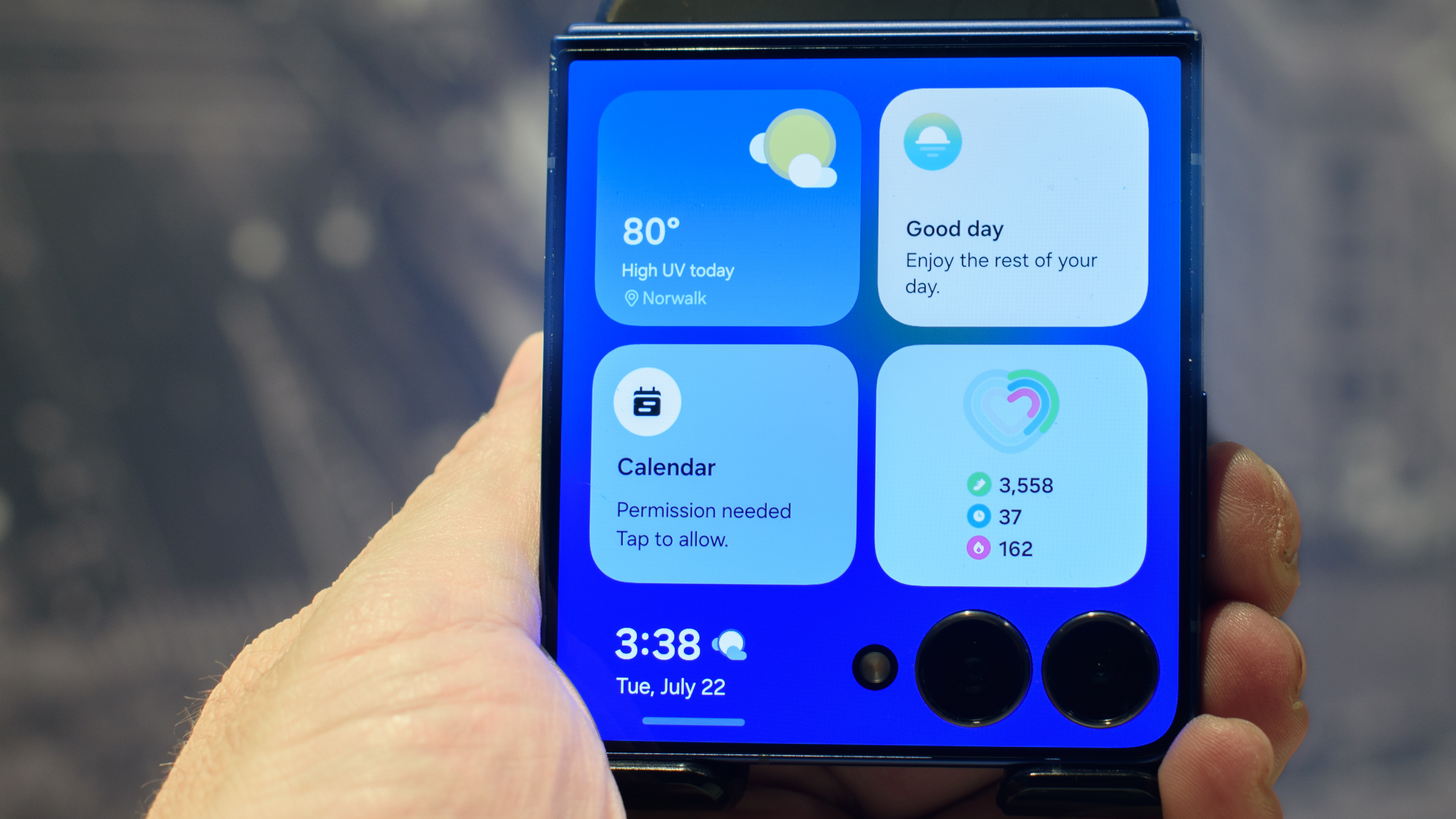 Samsung Galaxy Z Flip 7 in blue handheld showing four widgets on cover screen including weather, now brief, calendar and health monitor