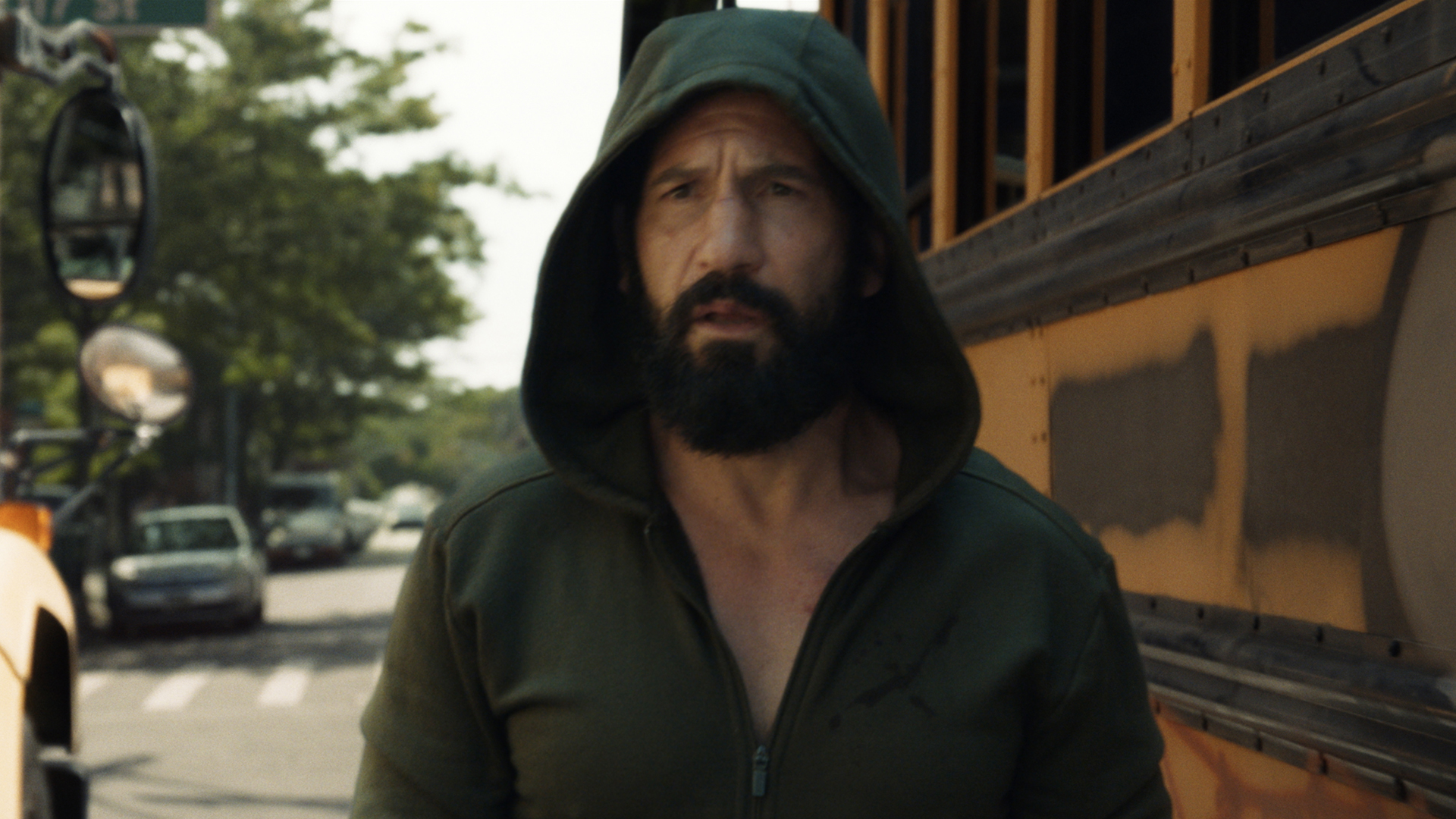 A hooded Frank Castle in front of an American school bus in The Punisher: One Last Kill